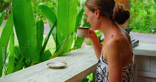 Girl smells and drinking hot morning Balinese coffee enjoying green tropical garden nature. Side view of lonely travel woman in Bali Island Nusa Penida Indonesia. Outdoor. photo