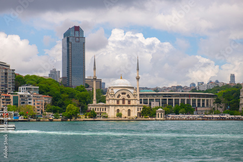 Dolmabahce Camii Mosque with Suzer Plaza building at the background at Bosporus strait waterside in Beyoglu district in historic city of Istanbul, Turkey.  photo