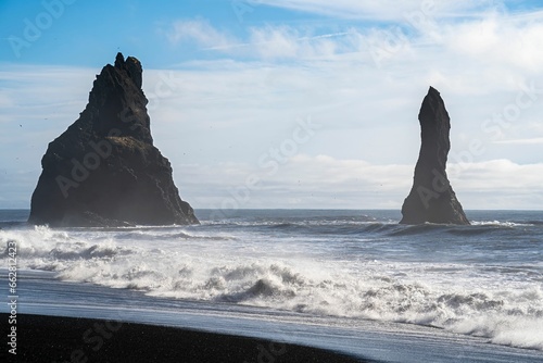 blacksand beach in Iceland with two basalt toweing rocks in the sea photo