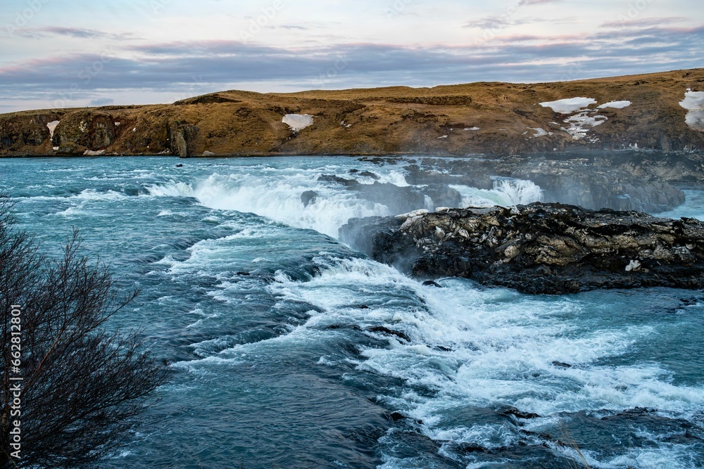 a body of water with a waterfall in it and a small island next to it,Urridafoss in icelan