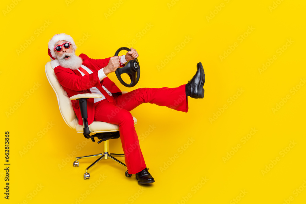 Full body portrait of impressed funky grandfather sit chair hands hold wheel isolated on yellow color background Full body portrait of impressed funky grandfather sit chair hands hold wheel isolated on yellow color background