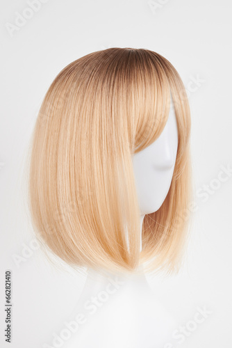 Natural looking blonde fair wig on white mannequin head. Short hair cut on the plastic wig holder isolated on white background, side view.