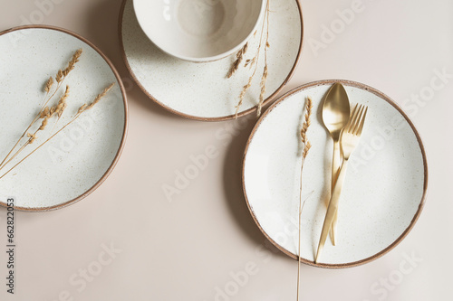 beige empty porcelain plate on pastel background with golden cutlery and dried flowers. Boho minimalist aesthetic. Dishware mock up. photo
