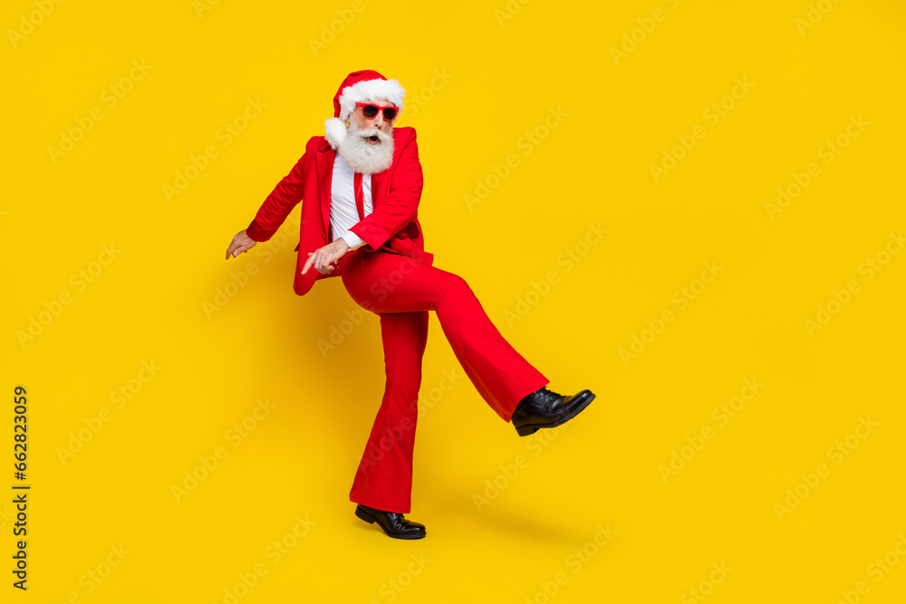 Full length photo of cute positive man pensioner dressed red suit santa hat having fun walking empty space isolated yellow color background Full length photo of cute positive man pensioner dressed red suit santa hat having fun walking empty space isolated yellow color background
