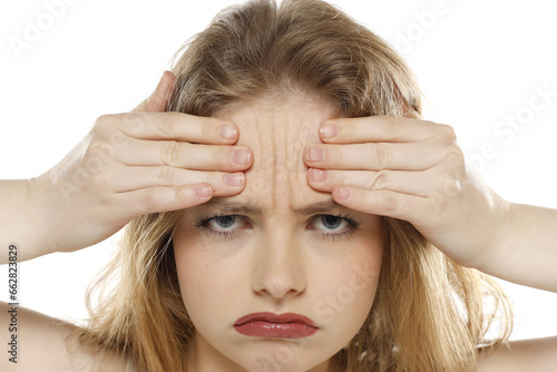 portrait of a young unhappy woman showing her wrinkles on her forehead on a white background