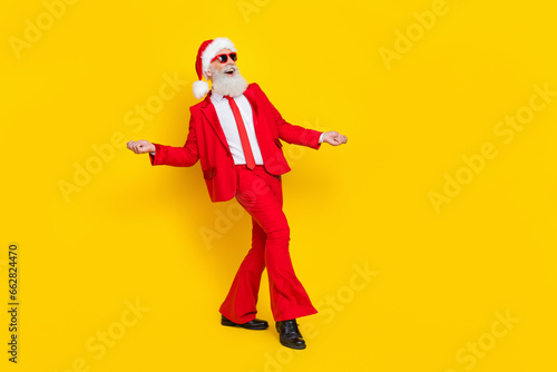 Full length photo of funky positive man pensioner dressed red suit santa hat having fun empty space isolated yellow color background © deagreez