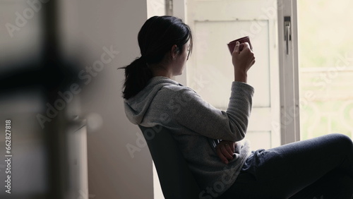 Foto Thoughtful woman sipping warm drink while staring out from home balcony window in contemplation