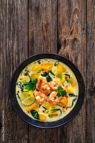 Thai soup with pumpkin, shrimps and coconut milk on wooden table
