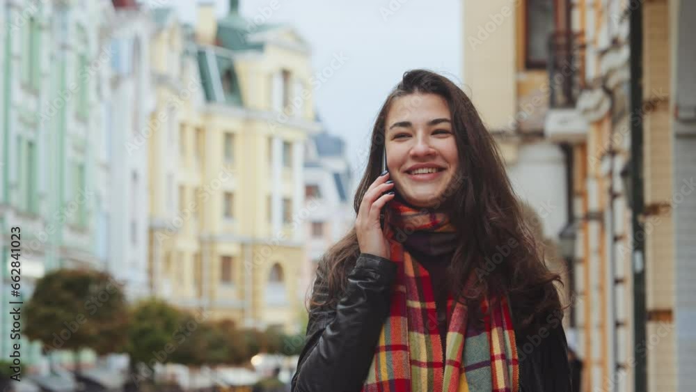 Portrait of attractive brunette, chatting cheerfully on her mobile phone outdoors. Young woman wearing leather jacket laughing contagiously at the news she heard. Mobile addiction concept Portrait of attractive brunette, chatting cheerfully on her mobile phone outdoors. Young woman wearing leather jacket laughing contagiously at the news she heard. Mobile addiction concept