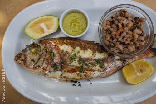 Delicious grilled whole sea bream with mustard sauce and citrus slices and small salad served on a plate in a greek tavern.