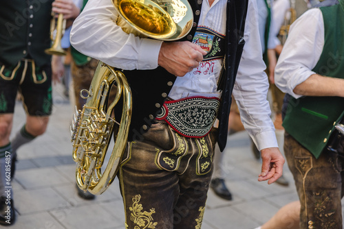 A man in traditional Bavarian attire carrying a wind instrument as part of a traditional brass band photo