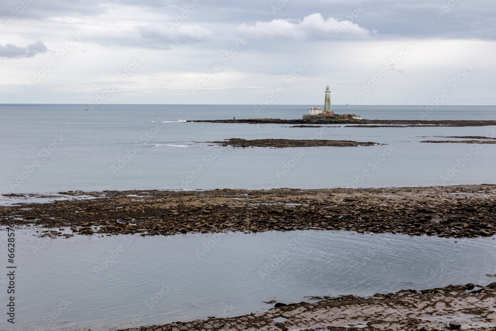 St. Mary's Lighthouse with basalt path at low tide with a series of basalt piers and a flat, calm sea just of the English coast. Whitley Bay, Newcastle, UK