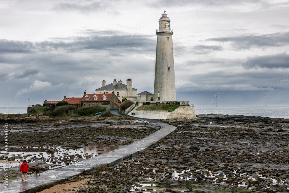 St. Mary's Lighthouse with basalt path at low tide with a large offshore windmill at sea, for alternative green, renewable energy, electricity, just of the English coast. Whitley Bay, Newcastle, UK