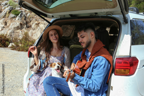 Happy hipster couple sitting in the trunk of the car and singing a song together with their rough coated jack russell terrier. Close up, copy space, background. © Evrymmnt