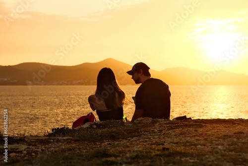 Silhouette of girl admiring beautiful sunset sitting on stone on sea coast. Silhouette of a man and a woman sitting on the seashore at sunset