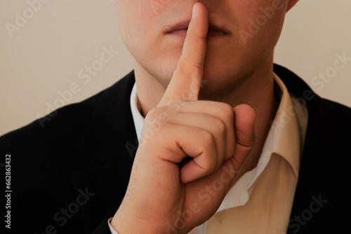 A person in a suit places their index finger to their lips in close-up. Silence sign, a request for silence, quiet behavior