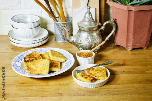 harcha or mbasses semolina algerian pancakes on an arabesque colorful plate. Traditional algerian breakfast bread with honey bowl and teapot photo