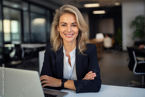 A professional business woman smiling at the camera sitting in a modern office with a laptop photo