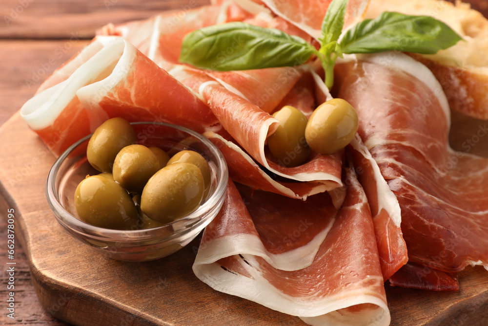 Slices of tasty cured ham, olives and basil on wooden board, closeup