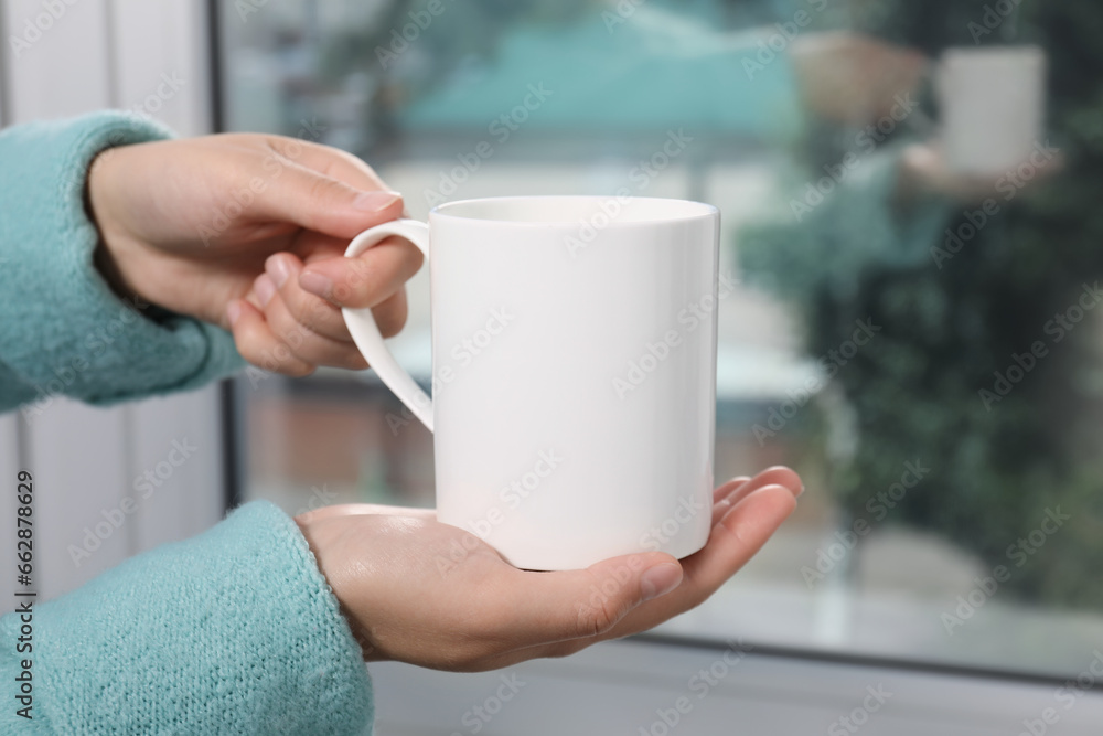 Woman holding white mug at home, closeup. Mockup for design Woman holding white mug at home, closeup. Mockup for design