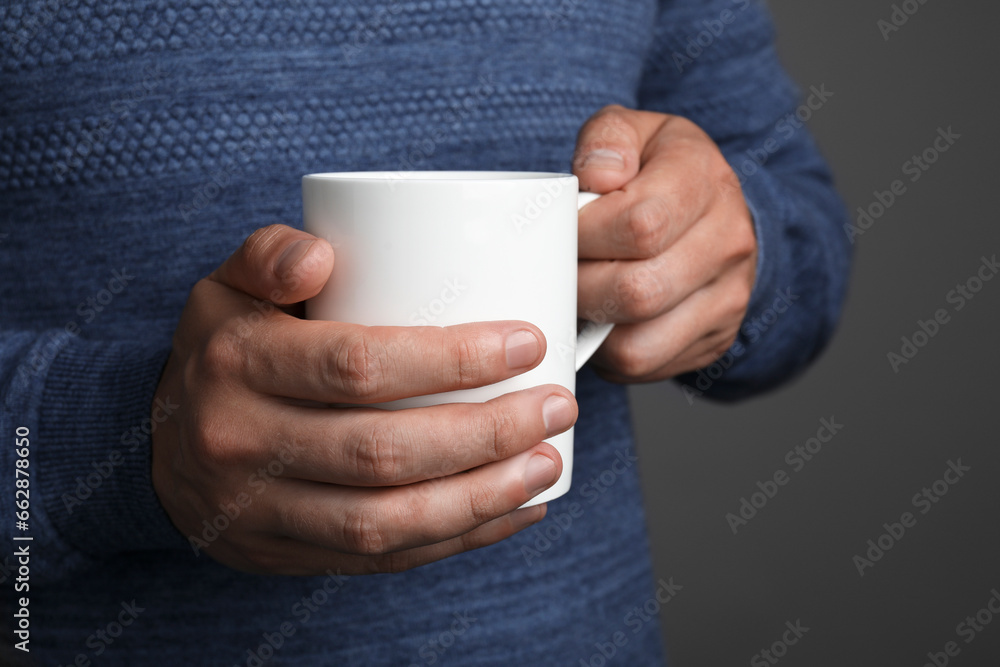 Man holding white mug on grey background, closeup Man holding white mug on grey background, closeup