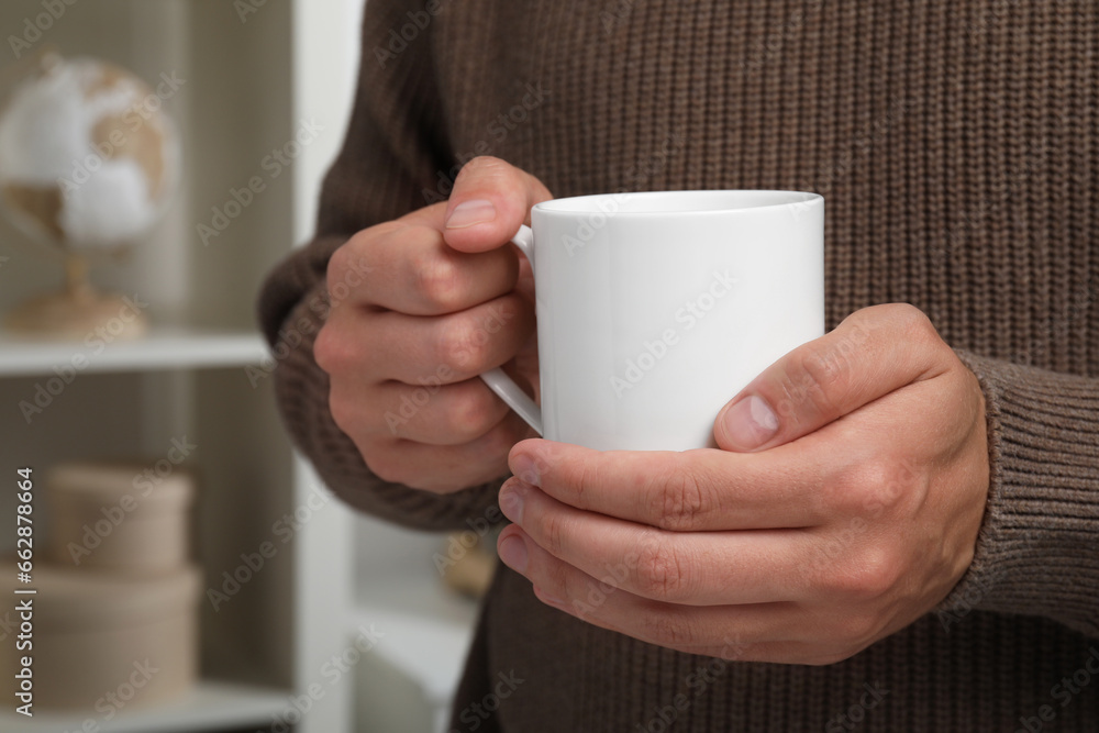 Man holding white mug indoors, closeup. Space for text Man holding white mug indoors, closeup. Space for text