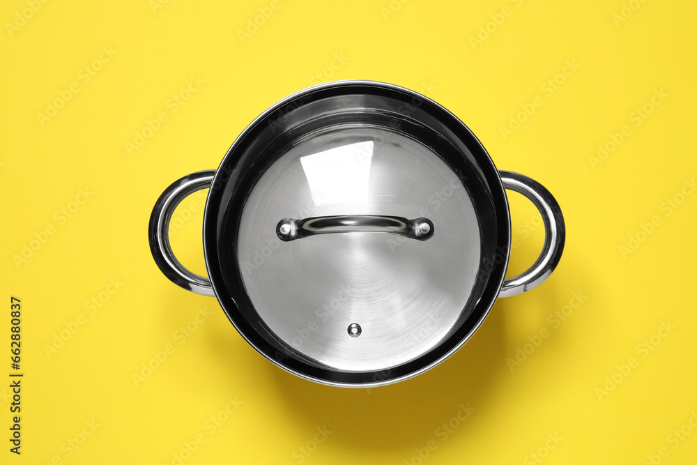 Steel pot with glass lid on yellow background, top view Steel pot with glass lid on yellow background, top view