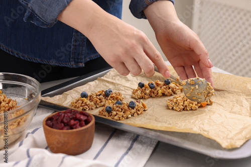 Making granola bars. Woman putting mixture of oat flakes, dry fruits and other ingredients onto baking tray at table in kitchen, closeup