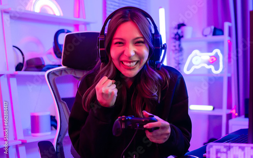 Beautiful happy young female game online streamer or caster smiling with fun, succeed for winner, using computer to play, sitting in room with decorated neon light. Looking at camera with copy space.