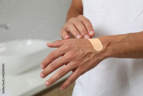 Man putting sticking plaster onto hand indoors, closeup © New Africa