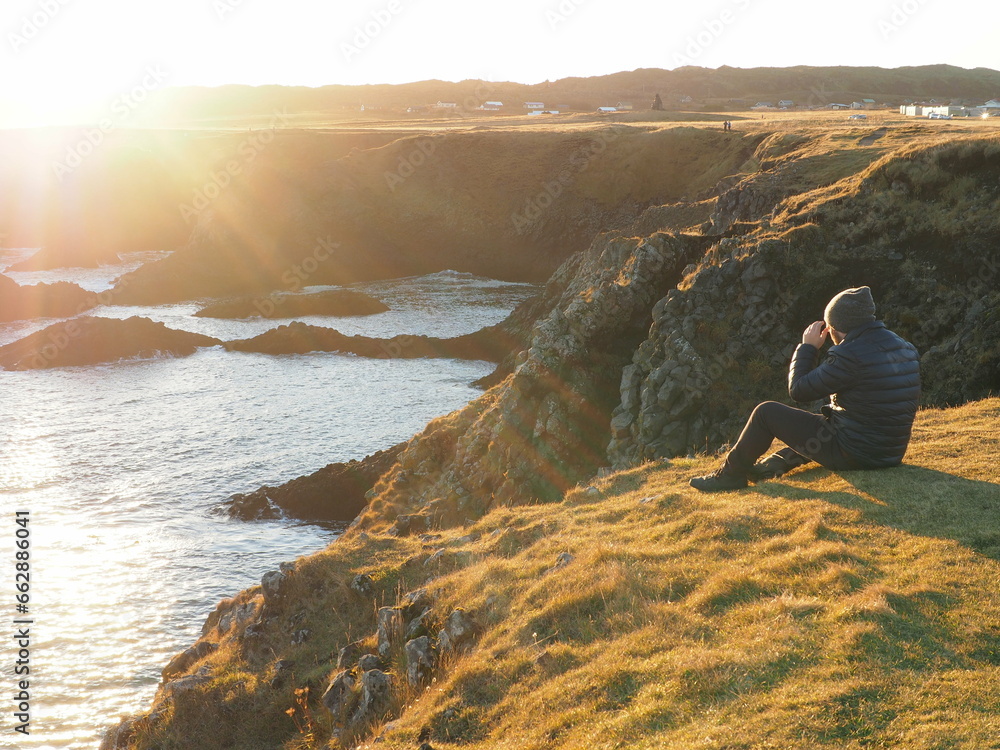A person sitting on the coast facing the sun, watching the sea, representing:  future, career development, opportunities, financial planning, investment return, financial stability
