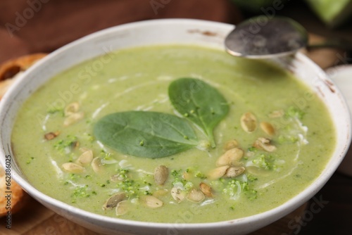 Delicious broccoli cream soup with basil and pumpkin seeds served on wooden table, closeup