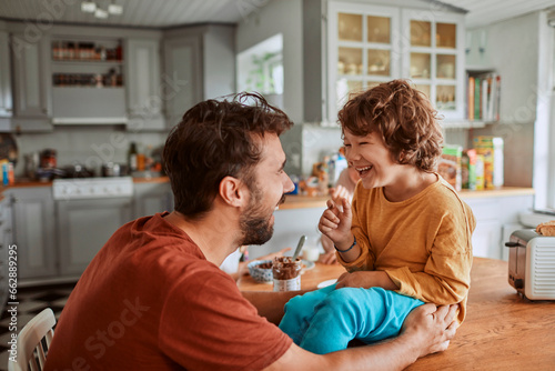 Young father and son being messy with chocolate spread in the kitchen at home