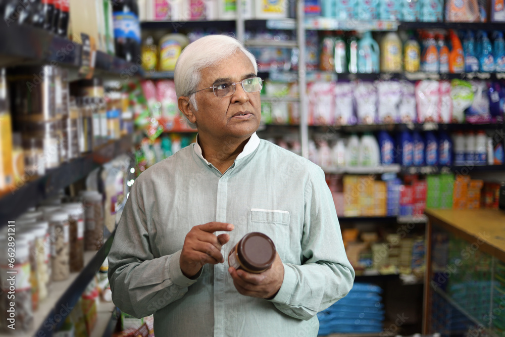 Old man standing in front of product shelf in grocery store. Confused old man buying grocery for home in supermarket. He is thinking and perplexed. Old man standing in front of product shelf in grocery store. Confused old man buying grocery for home in supermarket. He is thinking and perplexed.