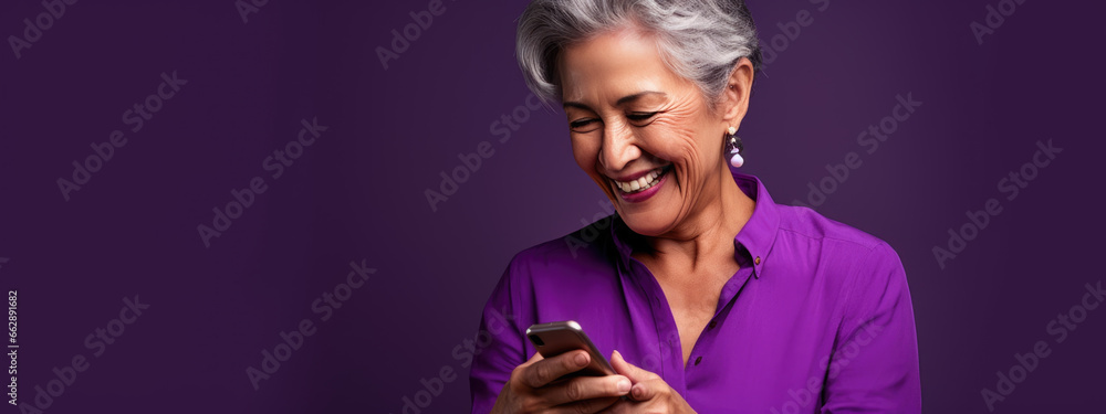 An elderly woman smiling and laughing with her phone against a colored background. - obrazy, fototapety, plakaty 