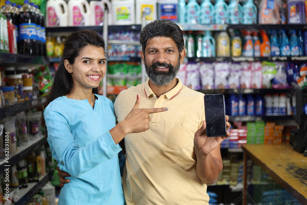 Happy Indian couple enjoying purchasing in grocery store. Buying grocery for home in supermarket. Pointing towards the mobile screen. Happy Indian couple enjoying purchasing in grocery store. Buying grocery for home in supermarket. Pointing towards the mobile screen.
