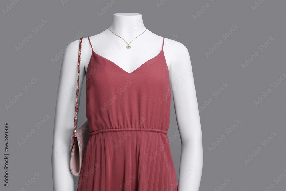 Female mannequin with necklace and bag dressed in stylish red dress on grey background Female mannequin with necklace and bag dressed in stylish red dress on grey background