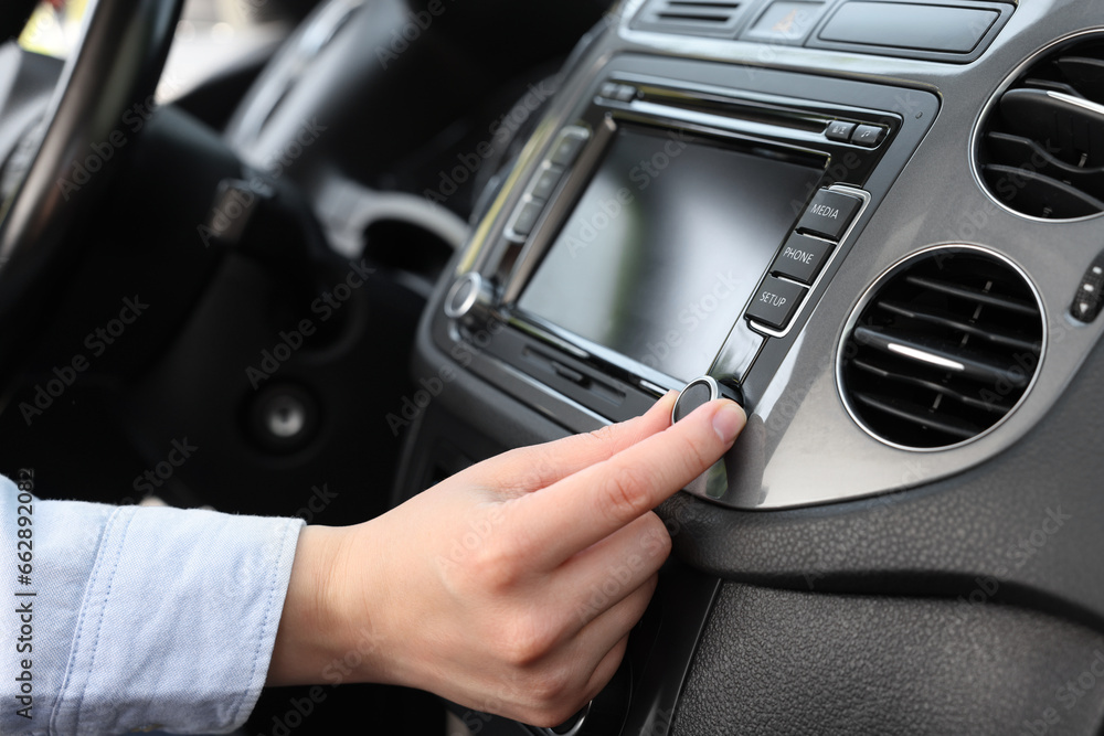 Listening to radio while driving. Woman turning volume button on vehicle audio in car, closeup