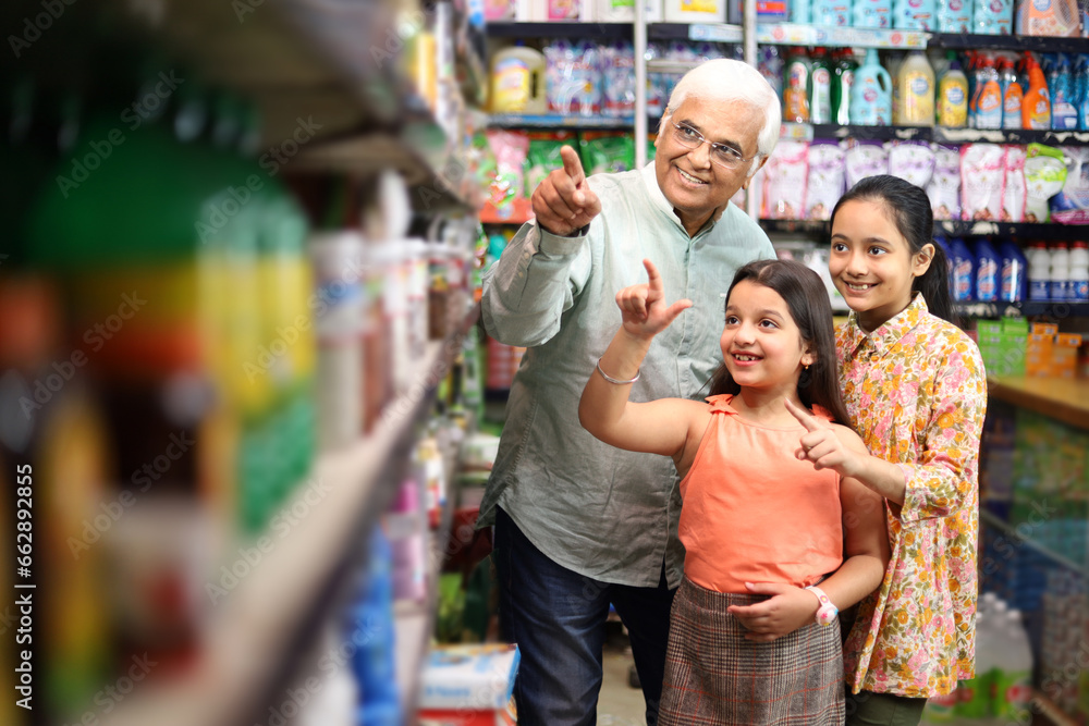 Happy Grandfather and Grand Daughters enjoying purchasing in grocery store. Buying grocery for home in supermarket. Grand daughters are happy with grandpa