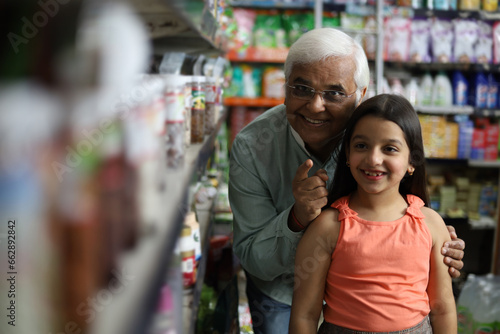 Happy Grandpa and Granddaughter enjoying purchasing in grocery store. Buying grocery for home in supermarket. Grandpa enjoying retirement with kid.