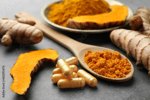 Aromatic turmeric powder, pills and raw roots on grey table, closeup