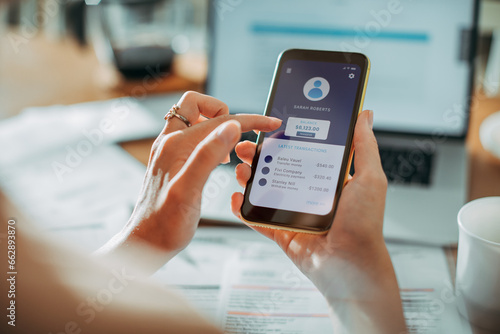 Young woman checking her profile on a bank app while paying bills at home photo