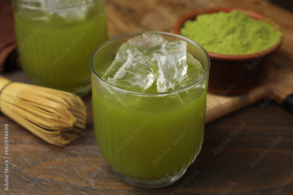 Glass of delicious iced green matcha tea, powder and bamboo whisk on wooden table, closeup Glass of delicious iced green matcha tea, powder and bamboo whisk on wooden table, closeup