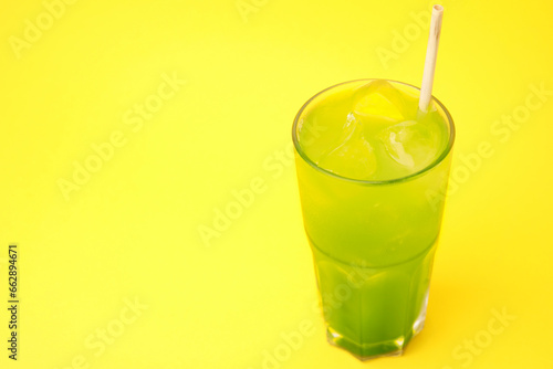 Glass of delicious iced green matcha tea on yellow background, space for text