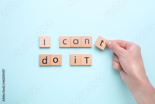 Fototapeta Naklejka Na Ścianę i Meble -  Motivation concept. Woman changing phrase from I Can't Do It into I Can Do It by removing wooden square with letter T on light blue background, top view
