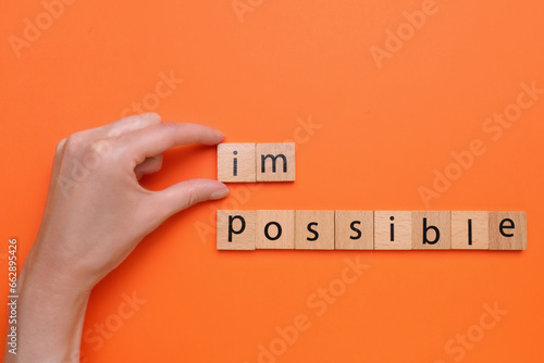 Motivation concept. Woman changing word from Impossible into Possible by removing wooden squares on orange background, top view