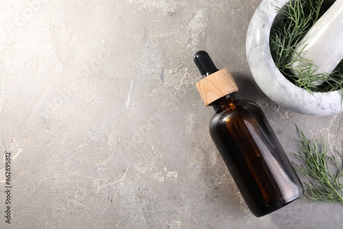 Bottle of essential oil and fresh dill on light gray textured table, flat lay. Space for text