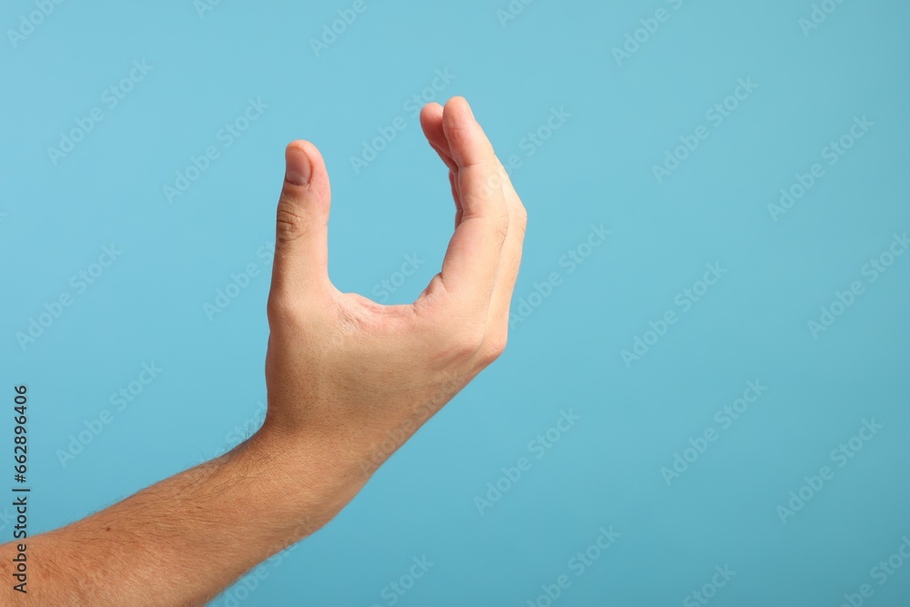 Man holding something in hand on light blue background, closeup. Space for text Man holding something in hand on light blue background, closeup. Space for text