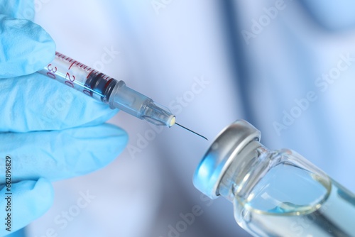 Doctor inserting syringe into glass vial with medication, closeup photo
