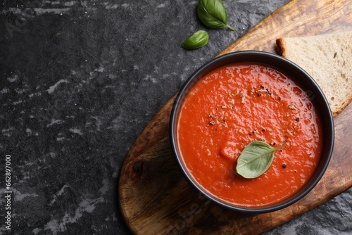 Obraz na plátně Delicious tomato cream soup in bowl and basil leaves on dark textured table, flat lay